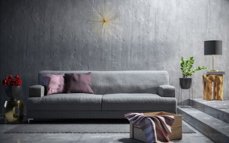 Modern eingerichtetes Wohnzimmer mit grauem Sofa, dekorativen Kissen, Betonstruktur-Wand und stilvollen Akzenten wie Stehlampe, Pflanze und Holzdetails